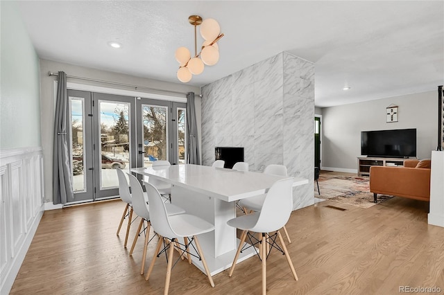 dining area with a chandelier, a fireplace, light hardwood / wood-style floors, and french doors