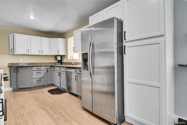 kitchen featuring dark stone countertops, light hardwood / wood-style floors, white cabinets, and appliances with stainless steel finishes