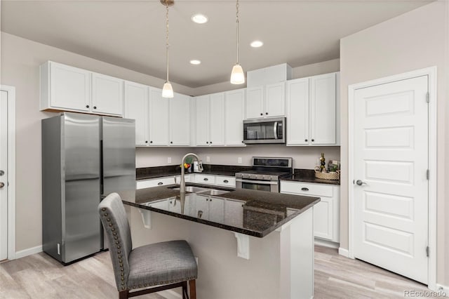9284 Gore St Unit A, Arvada, CO 80007 - kitchen featuring stainless steel appliances, light wood-style floors, white cabinets, dark stone counters, and decorative light fixtures