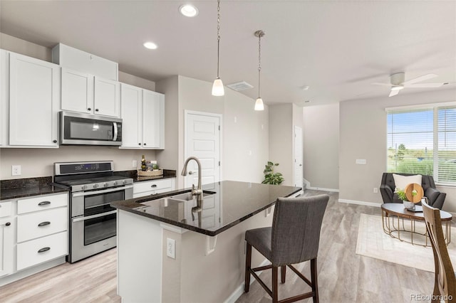 9284 Gore St Unit A, Arvada, CO 80007 - kitchen with appliances with stainless steel finishes, light wood-style floors, open floor plan, a center island with sink, and white cabinets