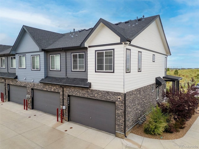 9284 Gore St Unit A, Arvada, CO 80007 - view of front of house featuring a shingled roof, an attached garage, driveway, and stone siding