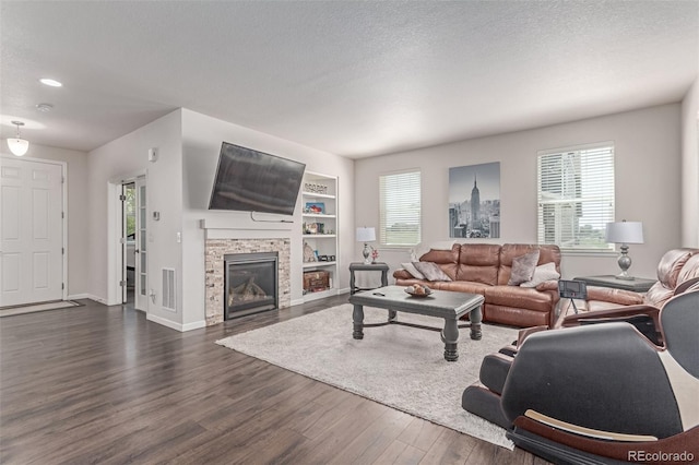 living room featuring dark wood-type flooring, a fireplace, baseboards, a textured ceiling, and built in shelves