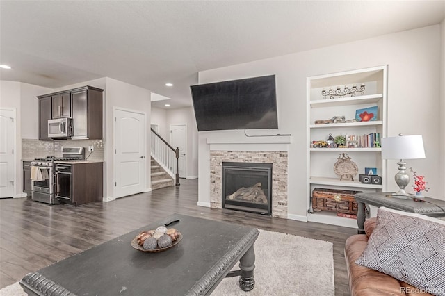 living area with dark wood finished floors, stairway, recessed lighting, a stone fireplace, and built in shelves