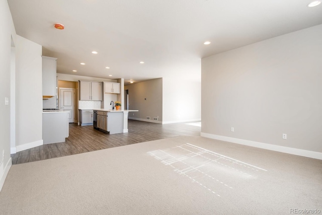 unfurnished living room featuring light wood finished floors, baseboards, recessed lighting, and a sink