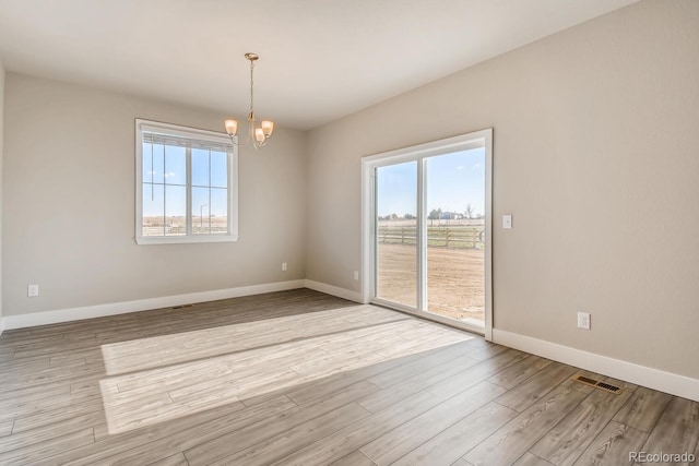 spare room featuring wood finished floors, visible vents, baseboards, and a notable chandelier
