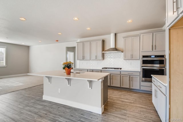 kitchen featuring wall chimney exhaust hood, stainless steel appliances, tasteful backsplash, light countertops, and a breakfast bar area