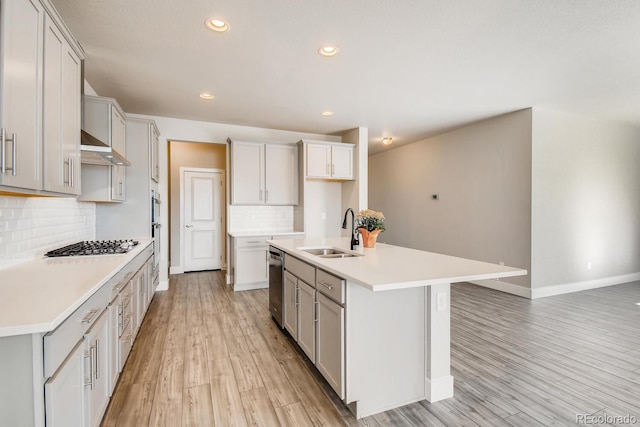 kitchen with backsplash, a sink, light wood-style floors, baseboards, and appliances with stainless steel finishes