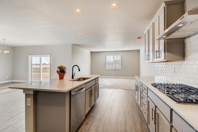 kitchen with stainless steel appliances, a sink, open floor plan, light wood-style floors, and wall chimney range hood