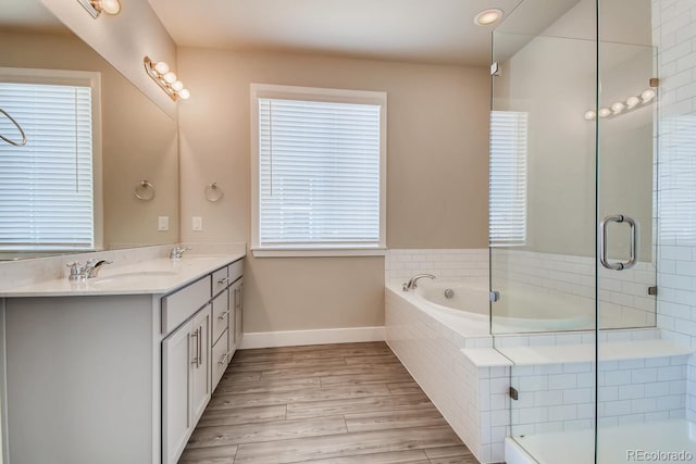 bathroom with a garden tub, wood finished floors, a sink, double vanity, and baseboards