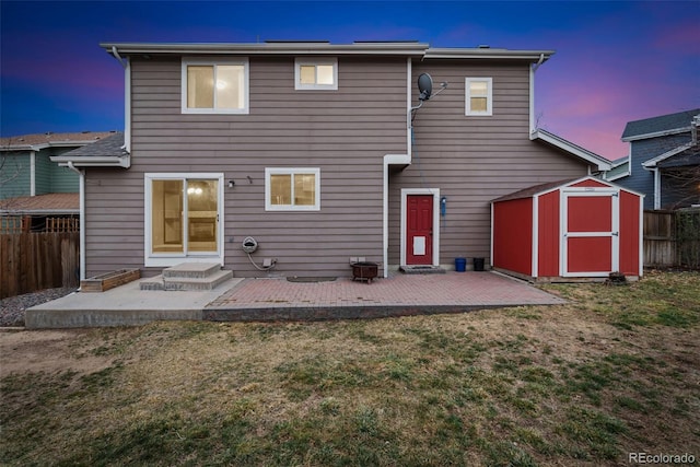 back of property at dusk with a yard, a patio area, fence, a shed, and an outdoor structure