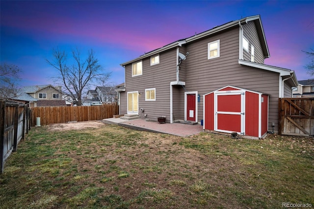 back of property at dusk with entry steps, a fenced backyard, a lawn, and a storage unit