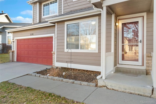 entrance to property featuring concrete driveway, a shingled roof, and an attached garage