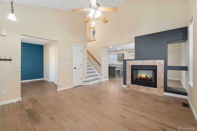 unfurnished living room with visible vents, stairway, light wood-style floors, a tile fireplace, and baseboards