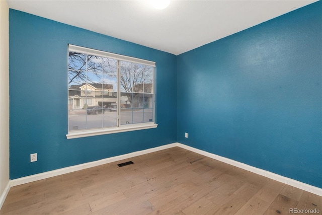 unfurnished room with hardwood / wood-style flooring, visible vents, and baseboards