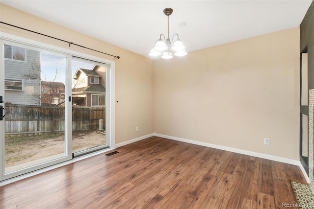 unfurnished room with a notable chandelier, wood finished floors, visible vents, and baseboards