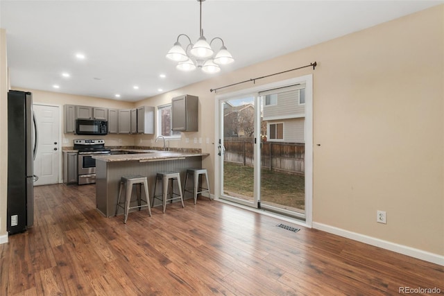 kitchen featuring dark wood-style floors, visible vents, gray cabinetry, appliances with stainless steel finishes, and a peninsula