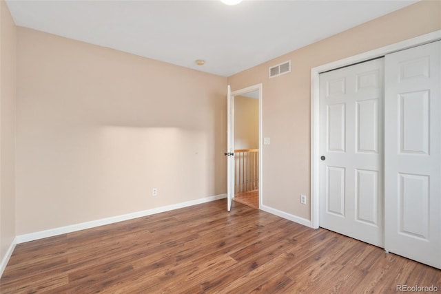 unfurnished bedroom with a closet, wood finished floors, visible vents, and baseboards