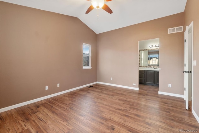 unfurnished bedroom with baseboards, visible vents, ensuite bath, wood finished floors, and vaulted ceiling