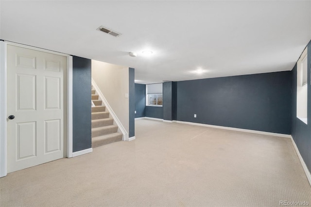 finished below grade area featuring visible vents, light carpet, baseboards, and stairs