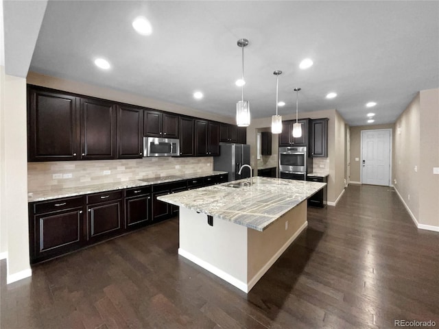 kitchen featuring sink, a center island with sink, pendant lighting, stainless steel appliances, and light stone countertops