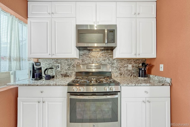 kitchen with white cabinetry, stainless steel appliances, light stone counters, and backsplash