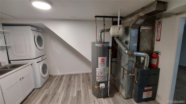 clothes washing area with a sink, gas water heater, cabinet space, light wood-style floors, and stacked washer / dryer