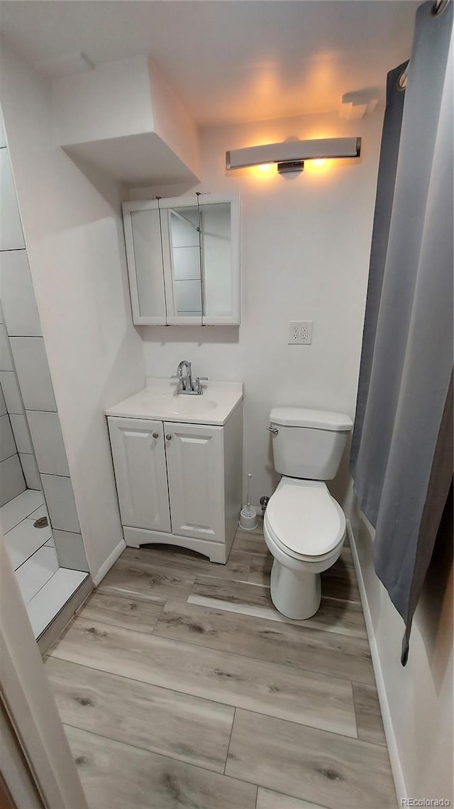 full bath featuring vanity, wood finished floors, baseboards, walk in shower, and toilet