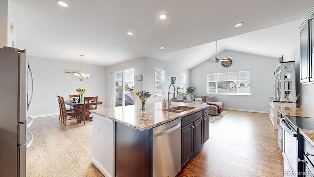 kitchen with sink, a kitchen island with sink, hanging light fixtures, stainless steel appliances, and light stone countertops