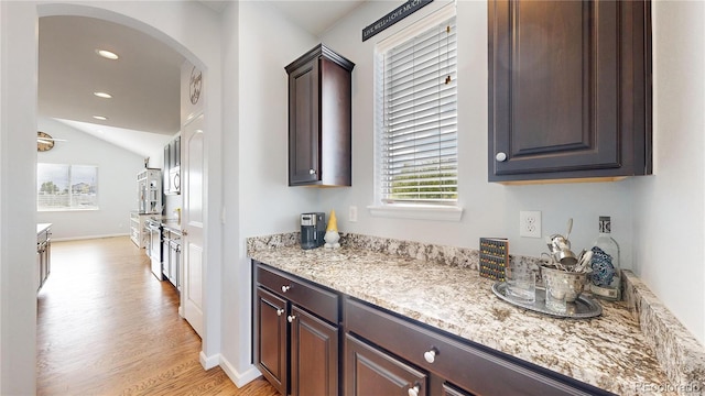 interior space with lofted ceiling, light stone countertops, dark brown cabinets, and light hardwood / wood-style flooring