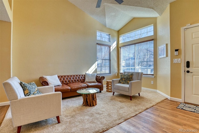 living room featuring ceiling fan, high vaulted ceiling, a textured ceiling, and light hardwood / wood-style floors