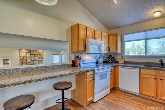 kitchen with a kitchen bar, lofted ceiling, a textured ceiling, light hardwood / wood-style flooring, and white appliances