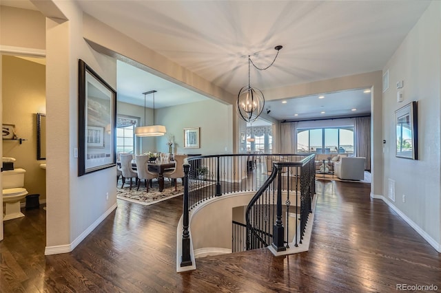corridor with wood finished floors, plenty of natural light, a chandelier, and an upstairs landing