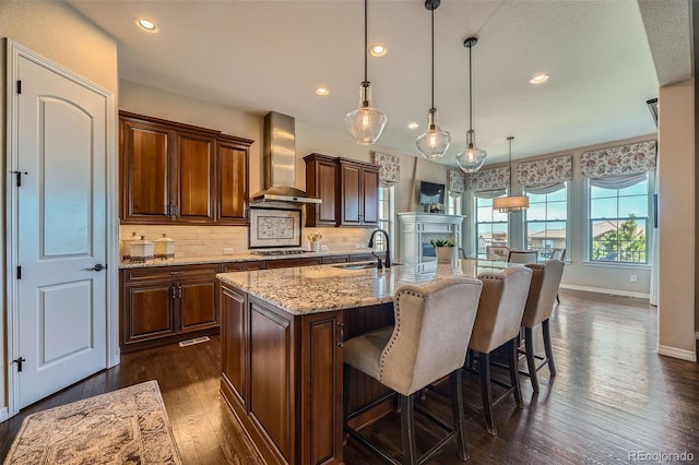 kitchen with dark wood-style floors, wall chimney exhaust hood, stovetop, tasteful backsplash, and a sink