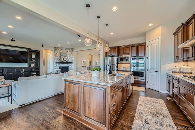 kitchen featuring decorative backsplash, appliances with stainless steel finishes, a fireplace, light stone countertops, and a sink