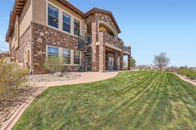 rear view of house with stone siding, a patio, stucco siding, stairs, and a yard