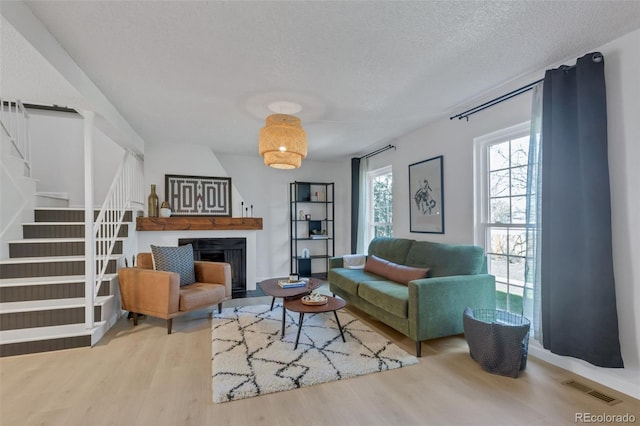living room with stairs, wood finished floors, a textured ceiling, and a fireplace