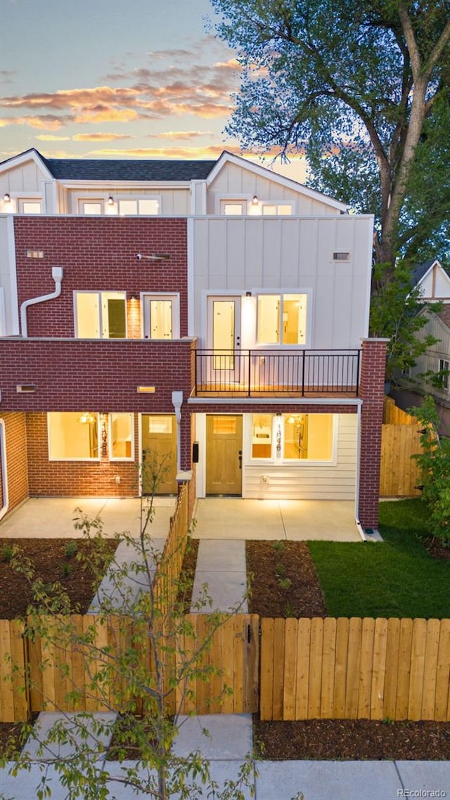 1046 N Knox Ct, Denver, CO 80204 - view of front facade with a fenced front yard, a balcony, brick siding, and board and batten siding