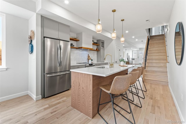 1046 N Knox Ct, Denver, CO 80204 - kitchen with appliances with stainless steel finishes, gray cabinetry, light wood-type flooring, tasteful backsplash, and a center island with sink