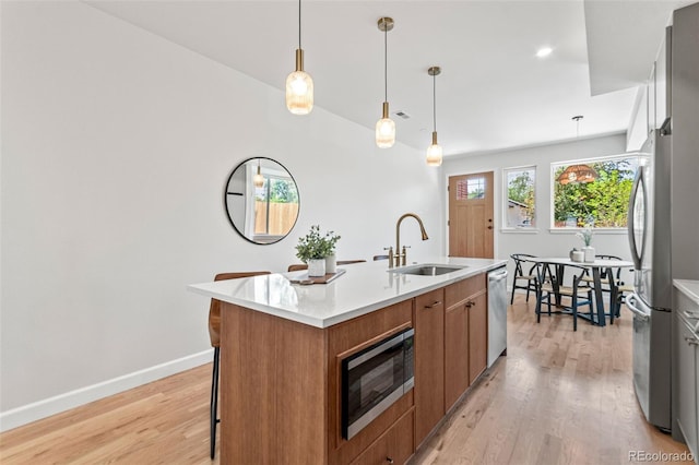 1046 N Knox Ct, Denver, CO 80204 - kitchen with appliances with stainless steel finishes, brown cabinetry, light wood-style floors, a kitchen island with sink, and light countertops