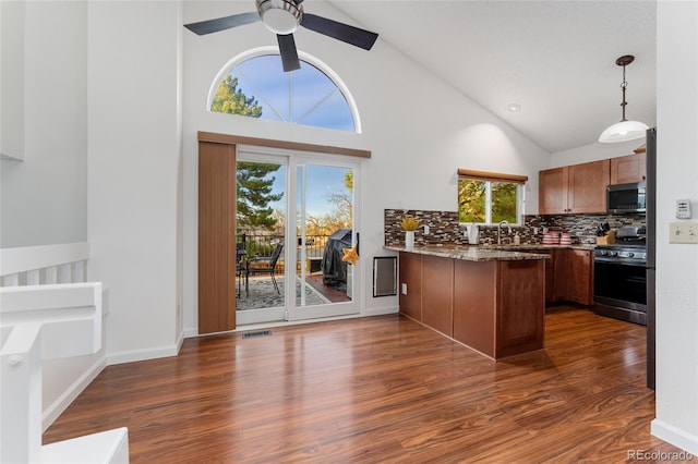 kitchen with kitchen peninsula, appliances with stainless steel finishes, dark wood-type flooring, high vaulted ceiling, and hanging light fixtures