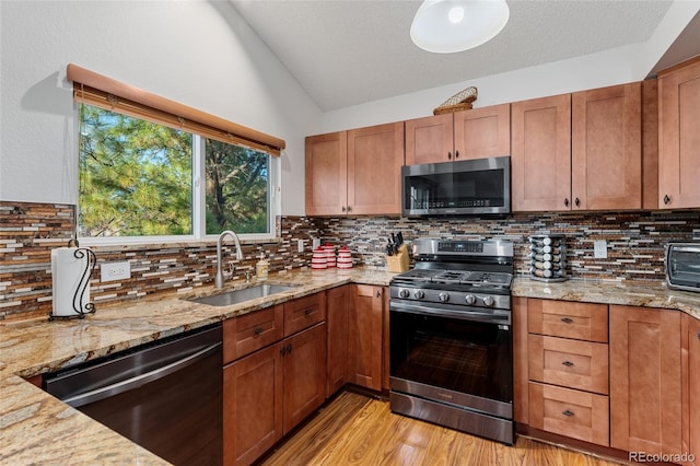 kitchen with decorative backsplash, appliances with stainless steel finishes, light stone countertops, and sink