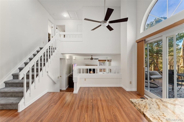 unfurnished living room featuring ceiling fan, wood-type flooring, and a high ceiling