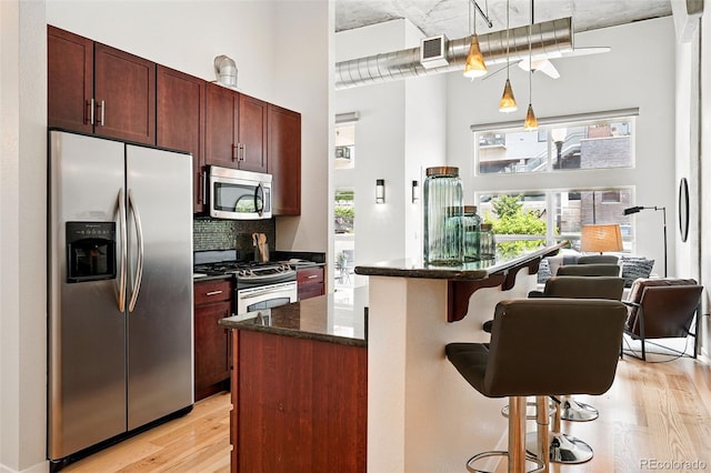 2518 16th St, Denver, CO 80211 - kitchen featuring appliances with stainless steel finishes, light wood finished floors, a high ceiling, decorative backsplash, and a breakfast bar