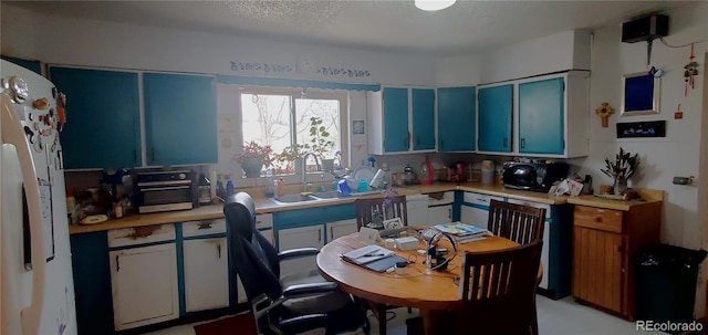 kitchen featuring blue cabinets, white appliances, a textured ceiling, and sink