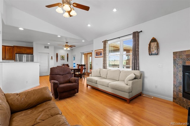 living room with lofted ceiling, light wood-type flooring, a tile fireplace, and ceiling fan