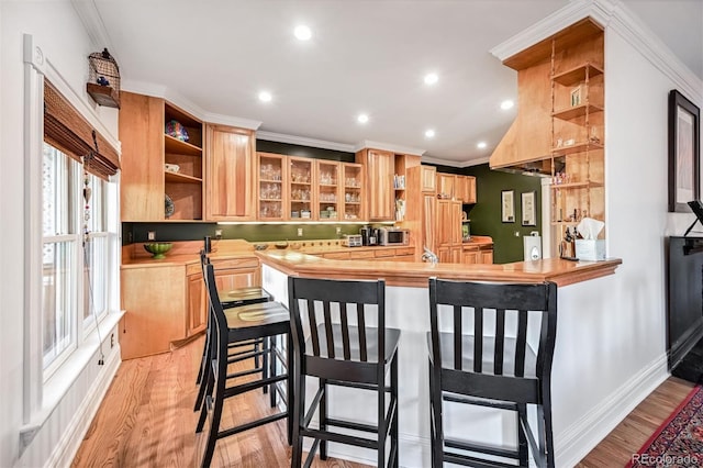 kitchen with wooden counters, light hardwood / wood-style flooring, ornamental molding, a kitchen breakfast bar, and kitchen peninsula