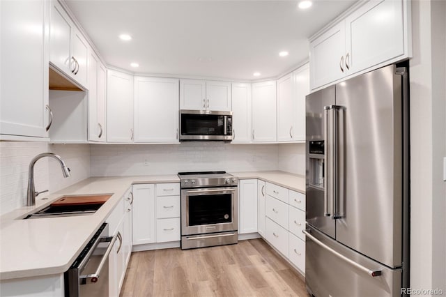 kitchen with sink, light wood-type flooring, appliances with stainless steel finishes, tasteful backsplash, and white cabinetry