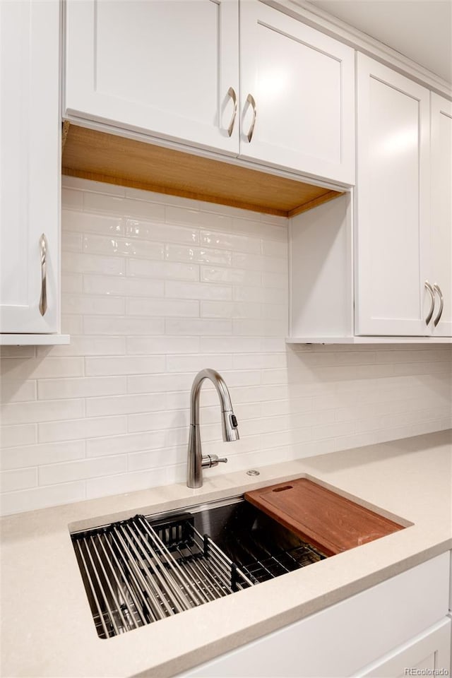 room details with decorative backsplash, white cabinetry, and sink