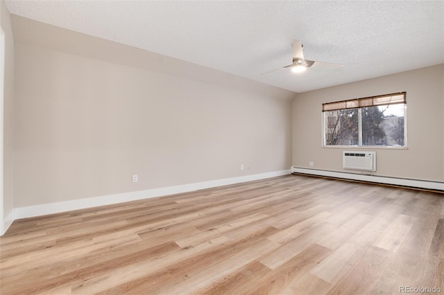 empty room with a wall mounted AC, ceiling fan, light hardwood / wood-style floors, and a textured ceiling