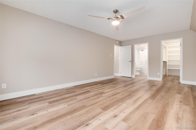 unfurnished bedroom with a walk in closet, ensuite bath, ceiling fan, a textured ceiling, and light hardwood / wood-style floors